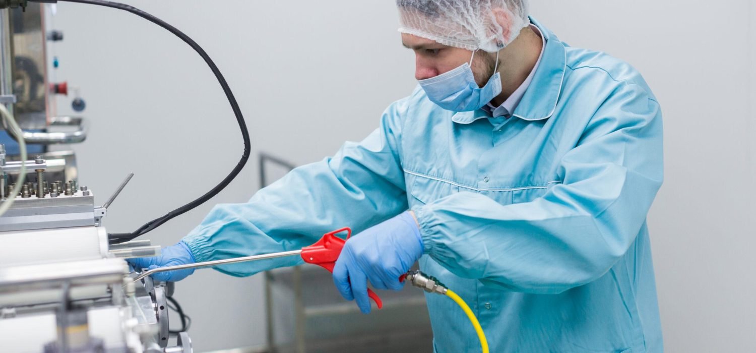 caucasian scientist in blue lab uniform configure manufacture machine with shafts and control panel, close picture