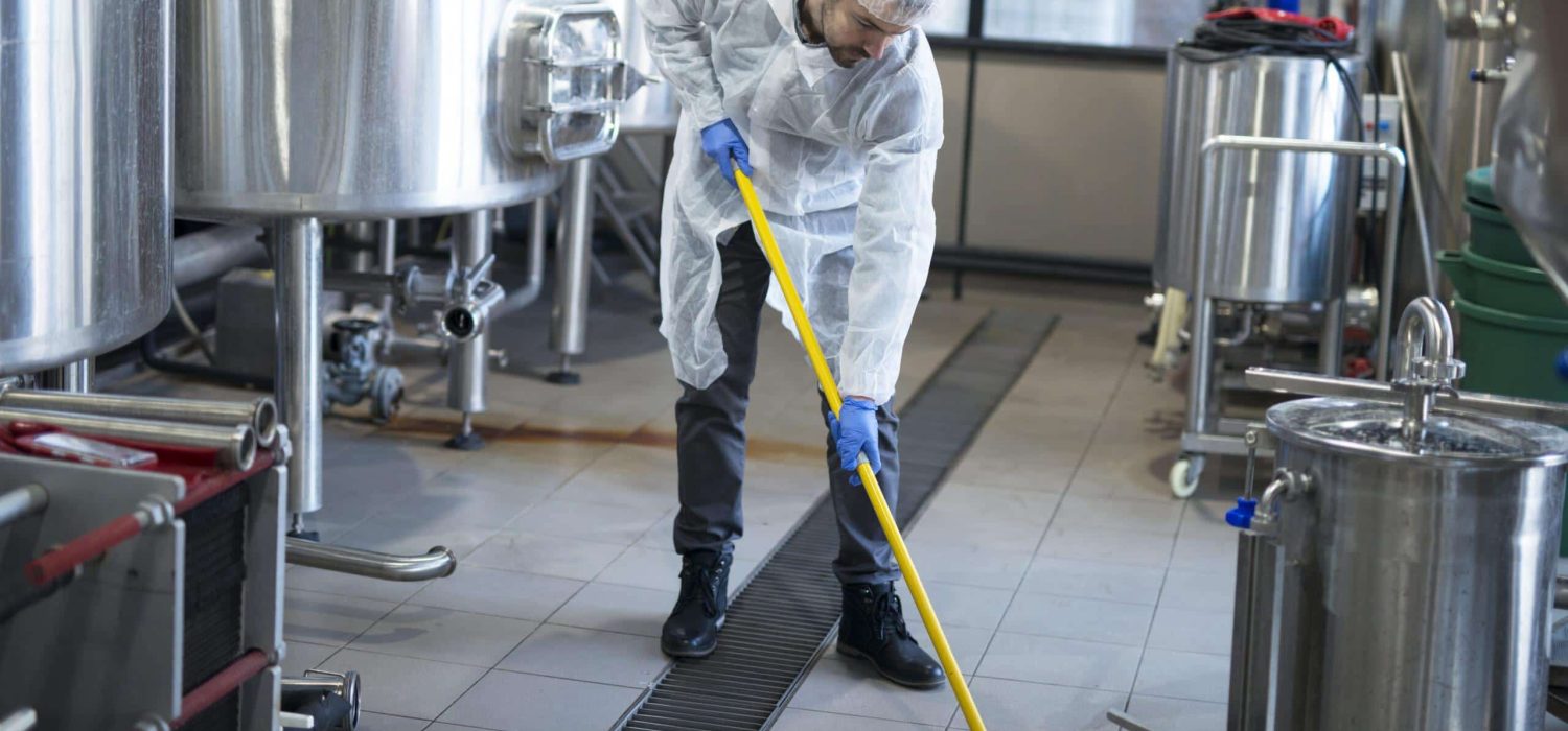 Professional cleaner wearing protection uniform cleaning floor of production plant.