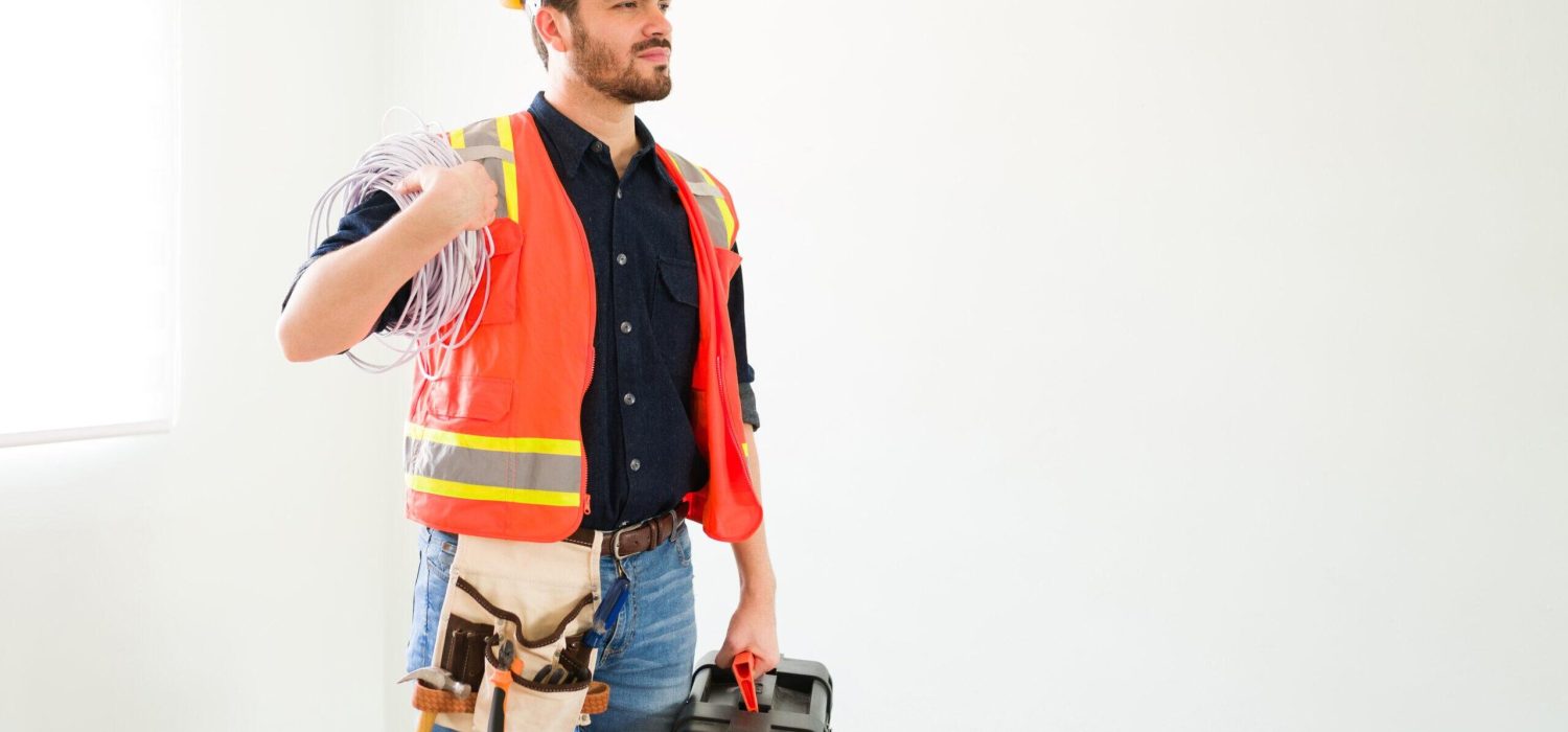 Ready to start my work. Proud attractive electrician with protective gear holding a toolbox and electricity cables