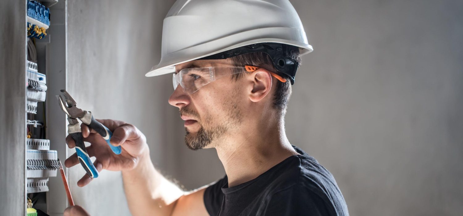 Man, an electrical technician working in a switchboard with fuses. Installation and connection of electrical equipment. Professional with tools in hand. concept of complex work, space for text.