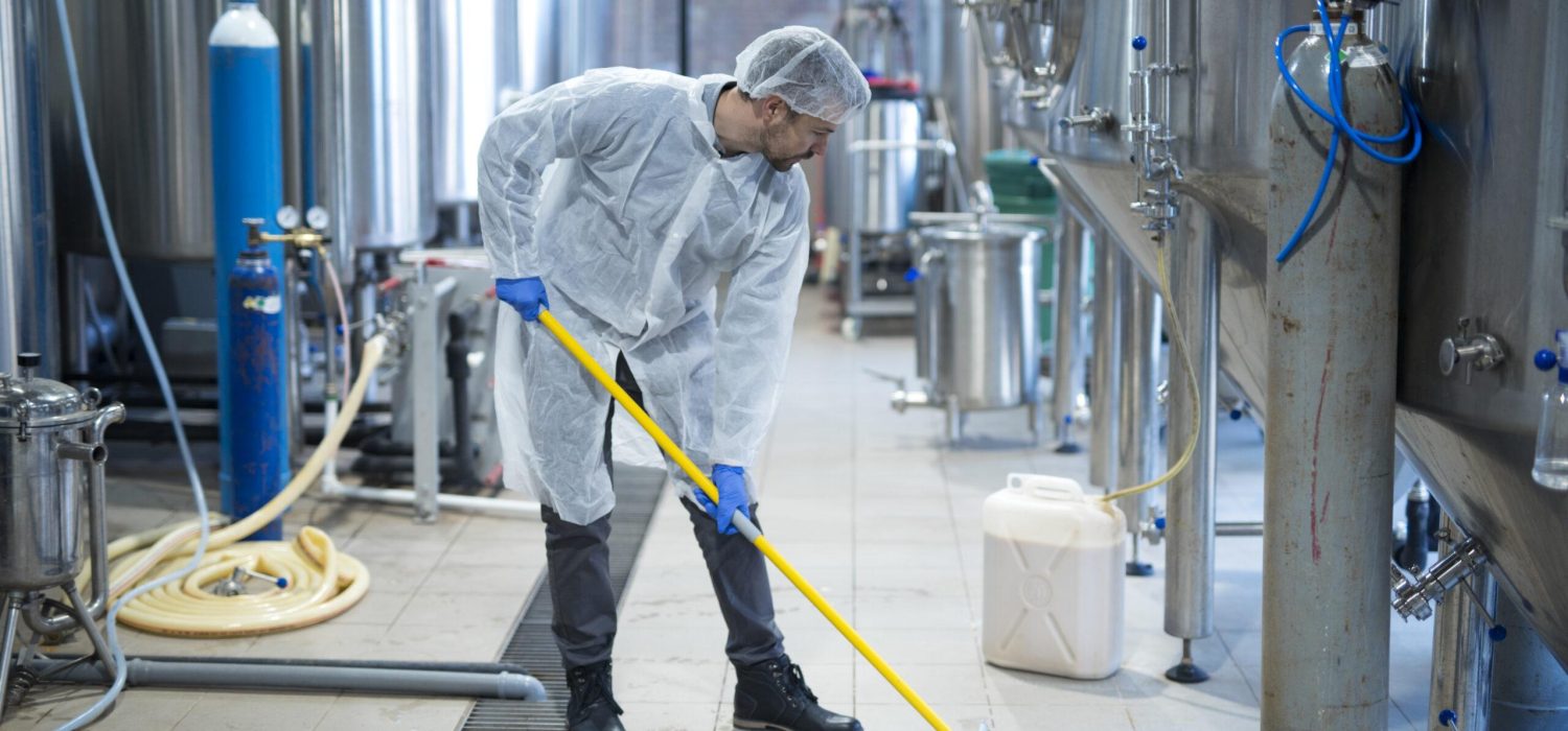 Professional industrial cleaner in protective uniform cleaning floor of food processing plant.